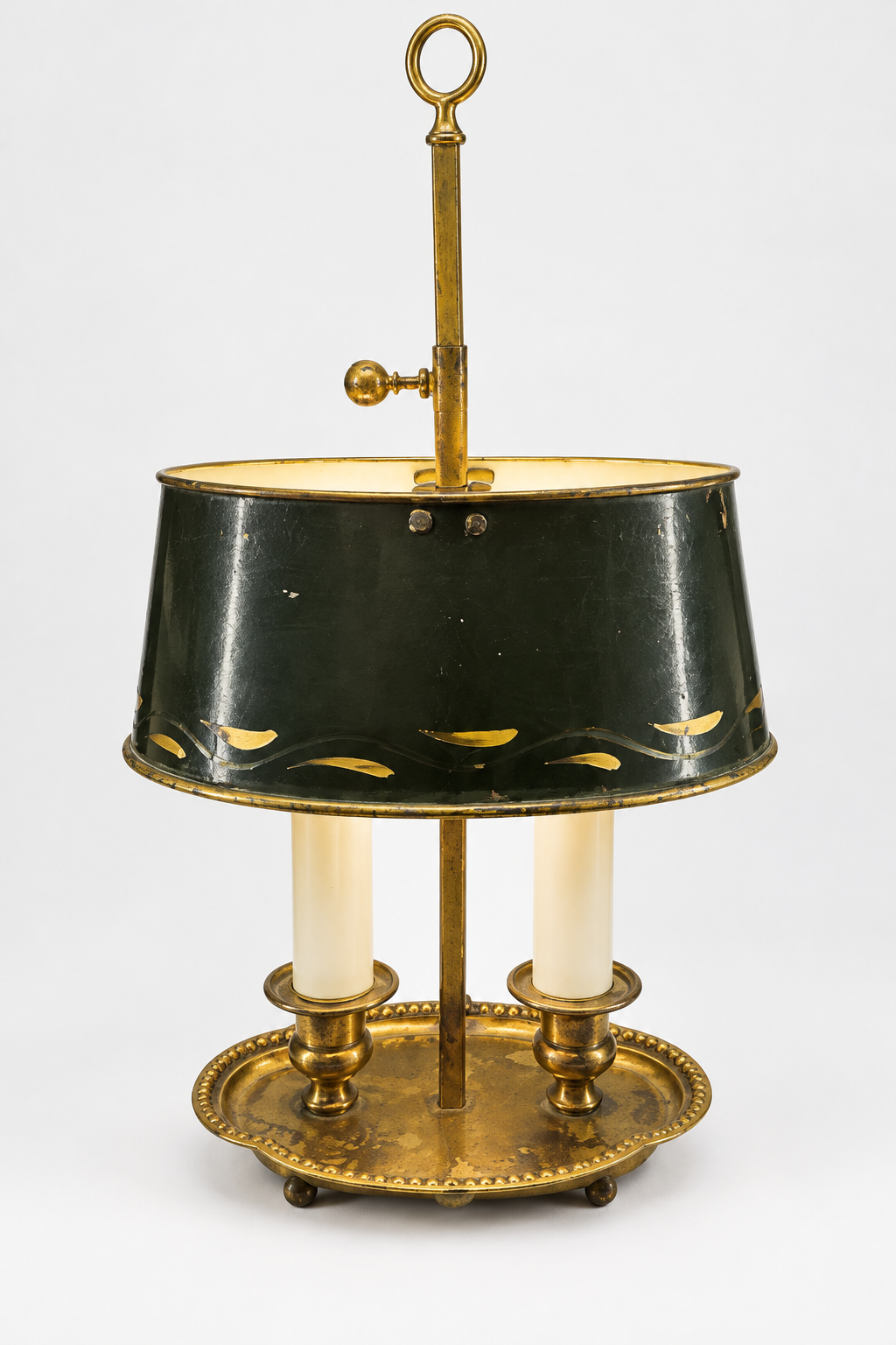 Antique two-light bouillotte lamp with dark green tole shade and original paint wear; standard ivory candle sleeves fitted before delivery