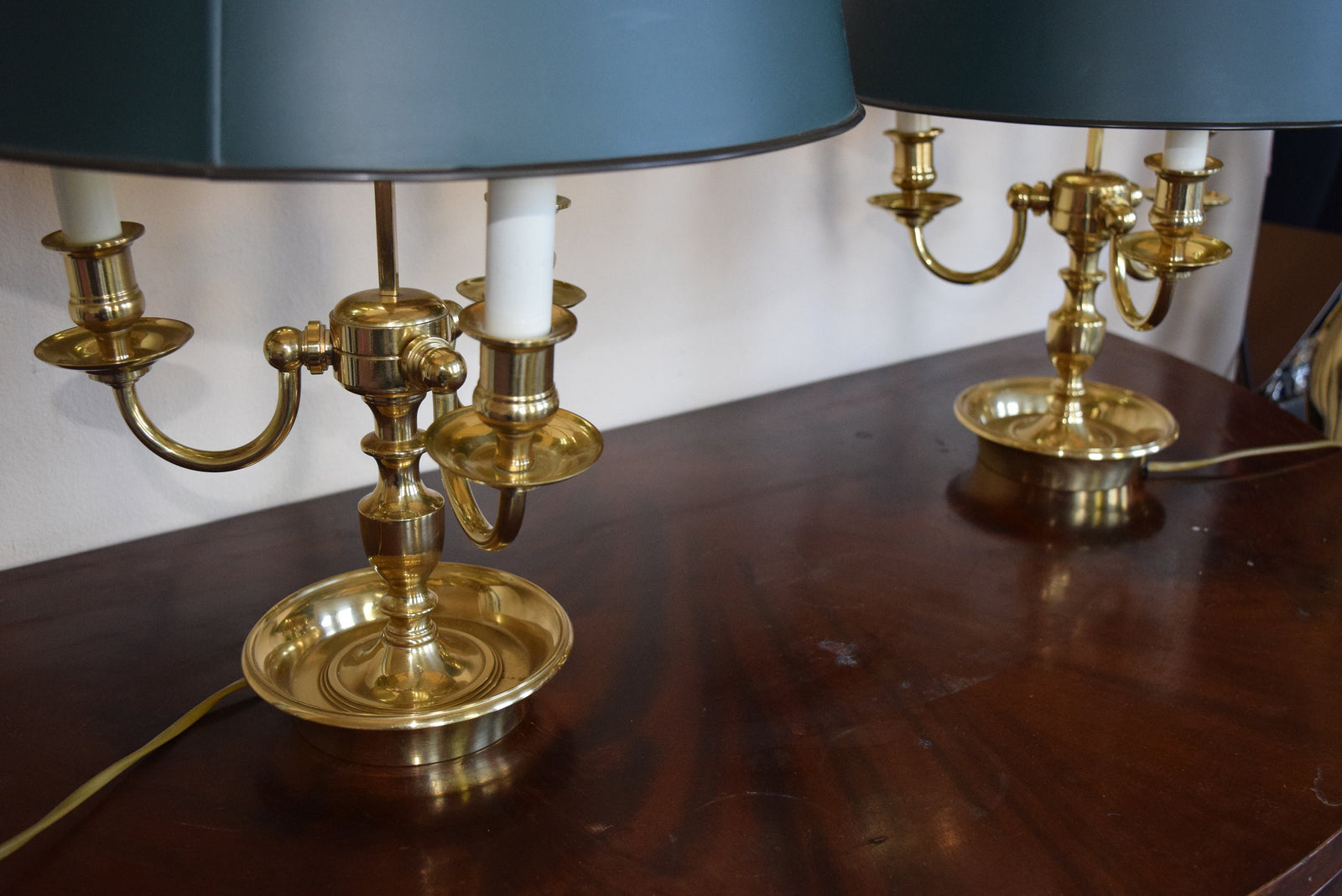 A pair of French Empire-style Bouillotte lamps with solid brass bases and deep green tole metal shades. Each lamp features three gracefully curved arms in a classic candelabra silhouette, exuding vintage sophistication. The adjustable shades allow for controlled lighting, perfect for desks, side tables, or elegant home decor. Ideal for lovers of antique lighting, French neoclassical design, and timeless statement pieces.