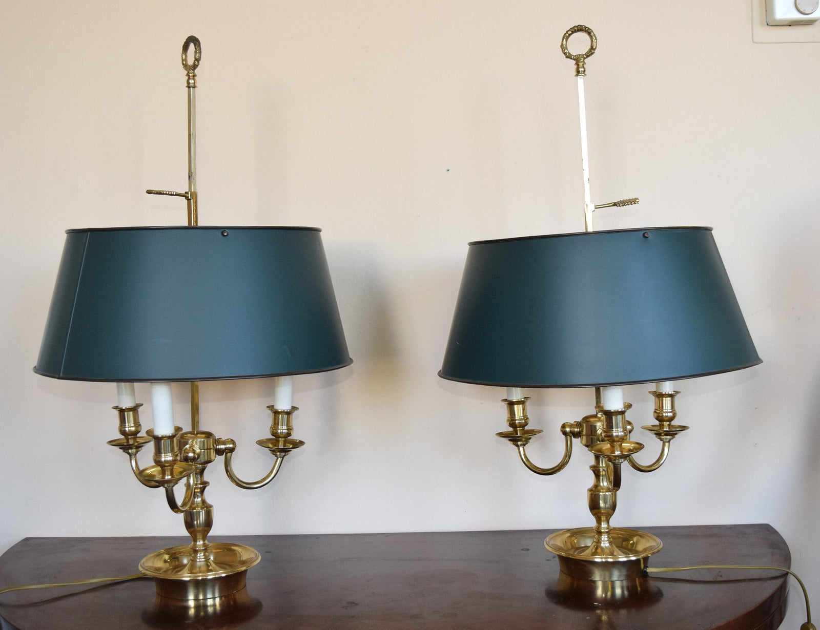 A pair of French Empire-style Bouillotte lamps with solid brass bases and deep green tole metal shades. Each lamp features three gracefully curved arms in a classic candelabra silhouette, exuding vintage sophistication. The adjustable shades allow for controlled lighting, perfect for desks, side tables, or elegant home decor. Ideal for lovers of antique lighting, French neoclassical design, and timeless statement pieces.