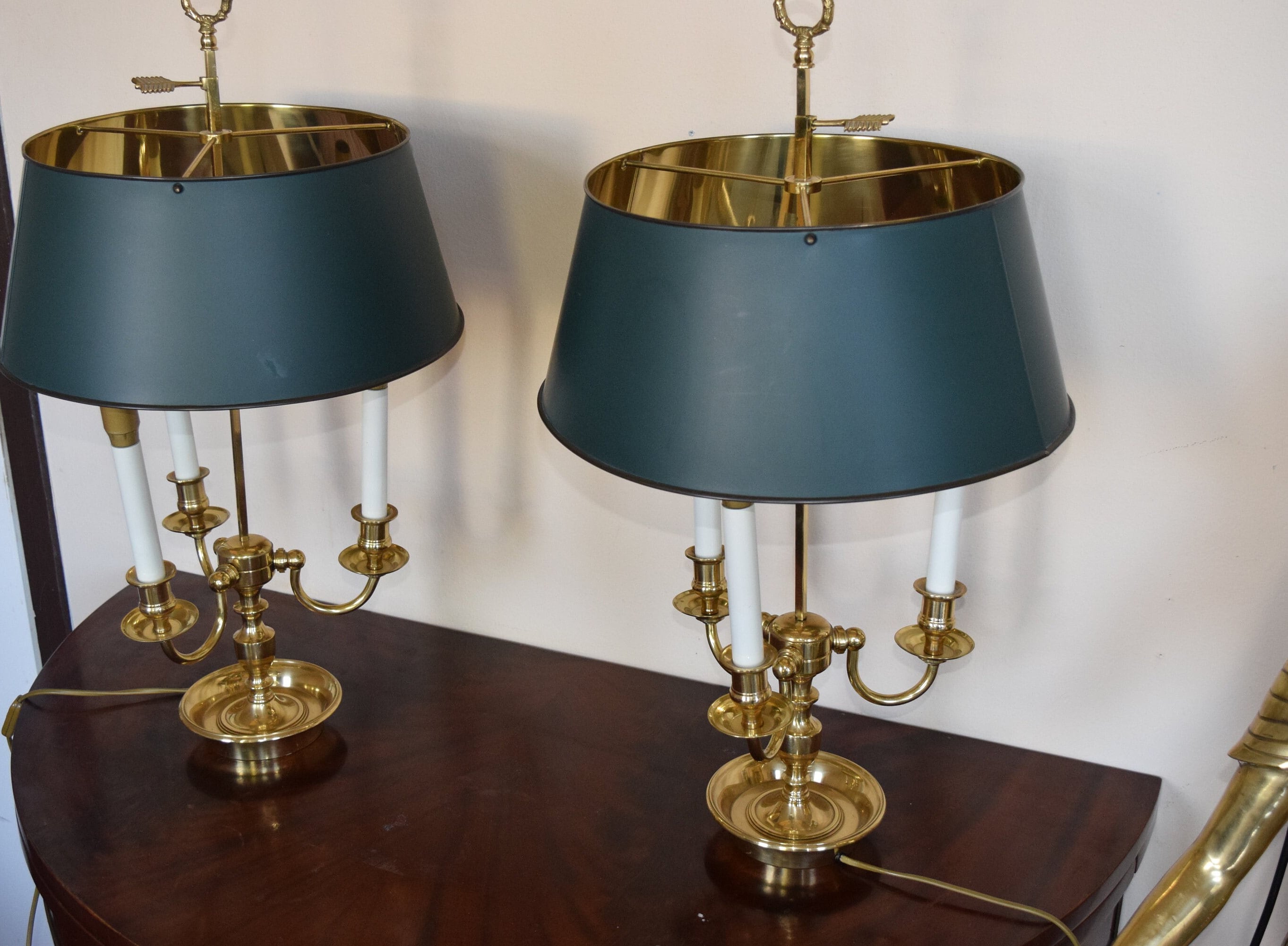 A pair of French Empire-style Bouillotte lamps with solid brass bases and deep green tole metal shades. Each lamp features three gracefully curved arms in a classic candelabra silhouette, exuding vintage sophistication. The adjustable shades allow for controlled lighting, perfect for desks, side tables, or elegant home decor. Ideal for lovers of antique lighting, French neoclassical design, and timeless statement pieces.