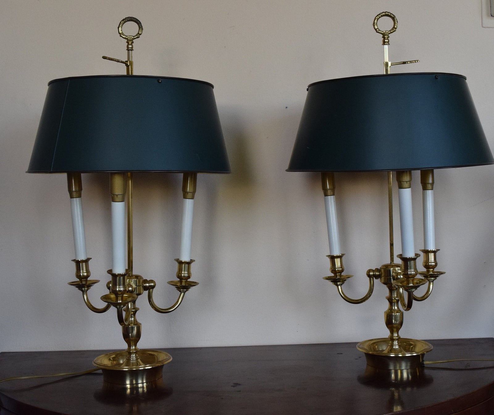 A pair of French Empire-style Bouillotte lamps with solid brass bases and deep green tole metal shades. Each lamp features three gracefully curved arms in a classic candelabra silhouette, exuding vintage sophistication. The adjustable shades allow for controlled lighting, perfect for desks, side tables, or elegant home decor. Ideal for lovers of antique lighting, French neoclassical design, and timeless statement pieces.