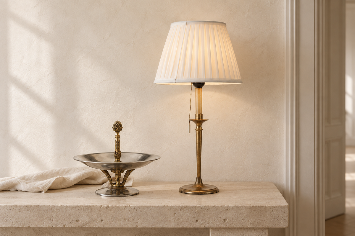 Styled interior illustration with a vintage brass lamp and silver-toned pedestal bowl from the collection